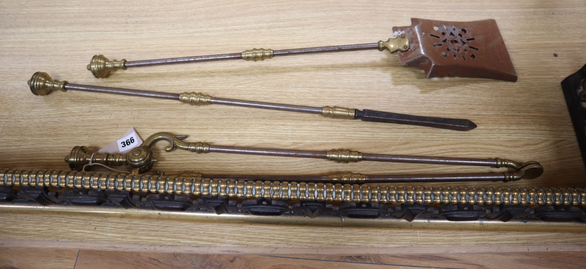 A Victorian brass and cast iron pierced fender and a three-piece set of later fire irons